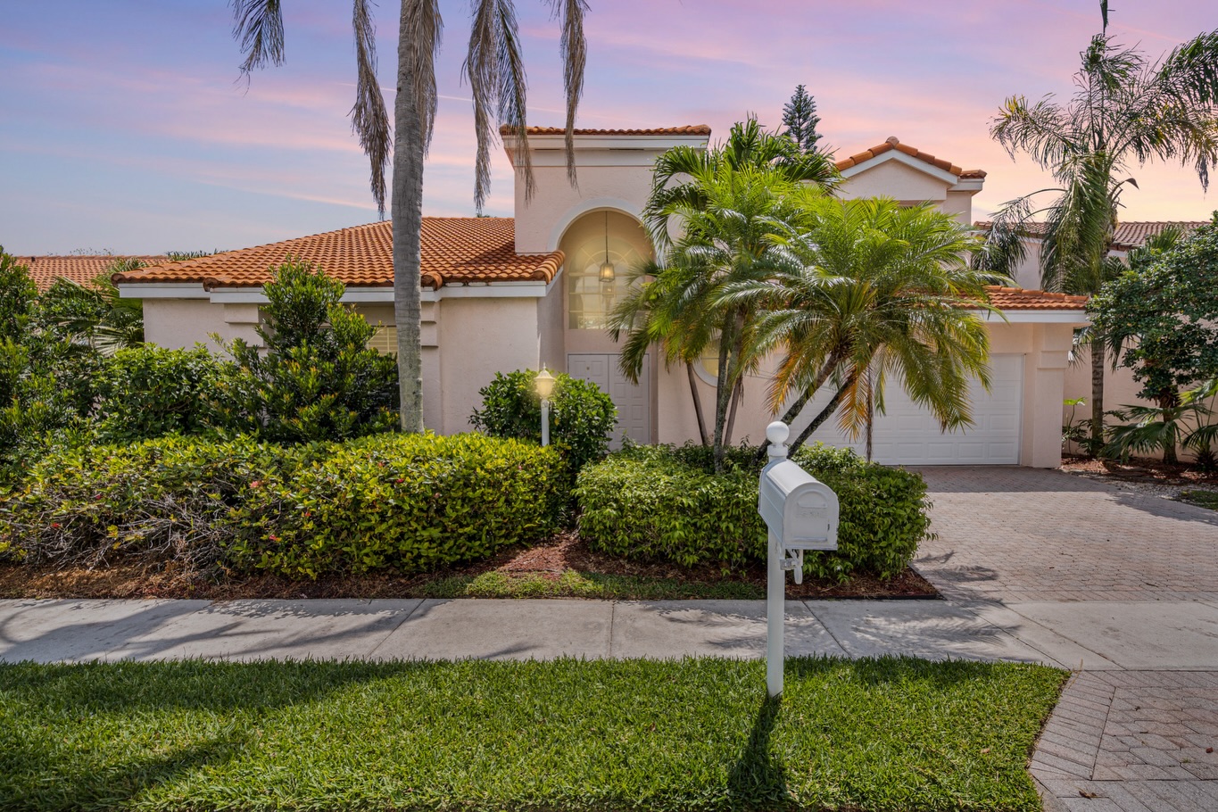 Mediterranean-style Florida estate photographed at twilight with palm trees and warm sunset sky